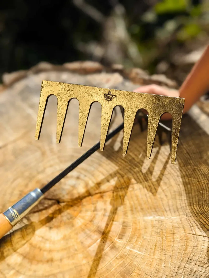 Hand Rake hand forged by Homestead Iron with bright sunlight on steel with harsh shadows on wooden background.