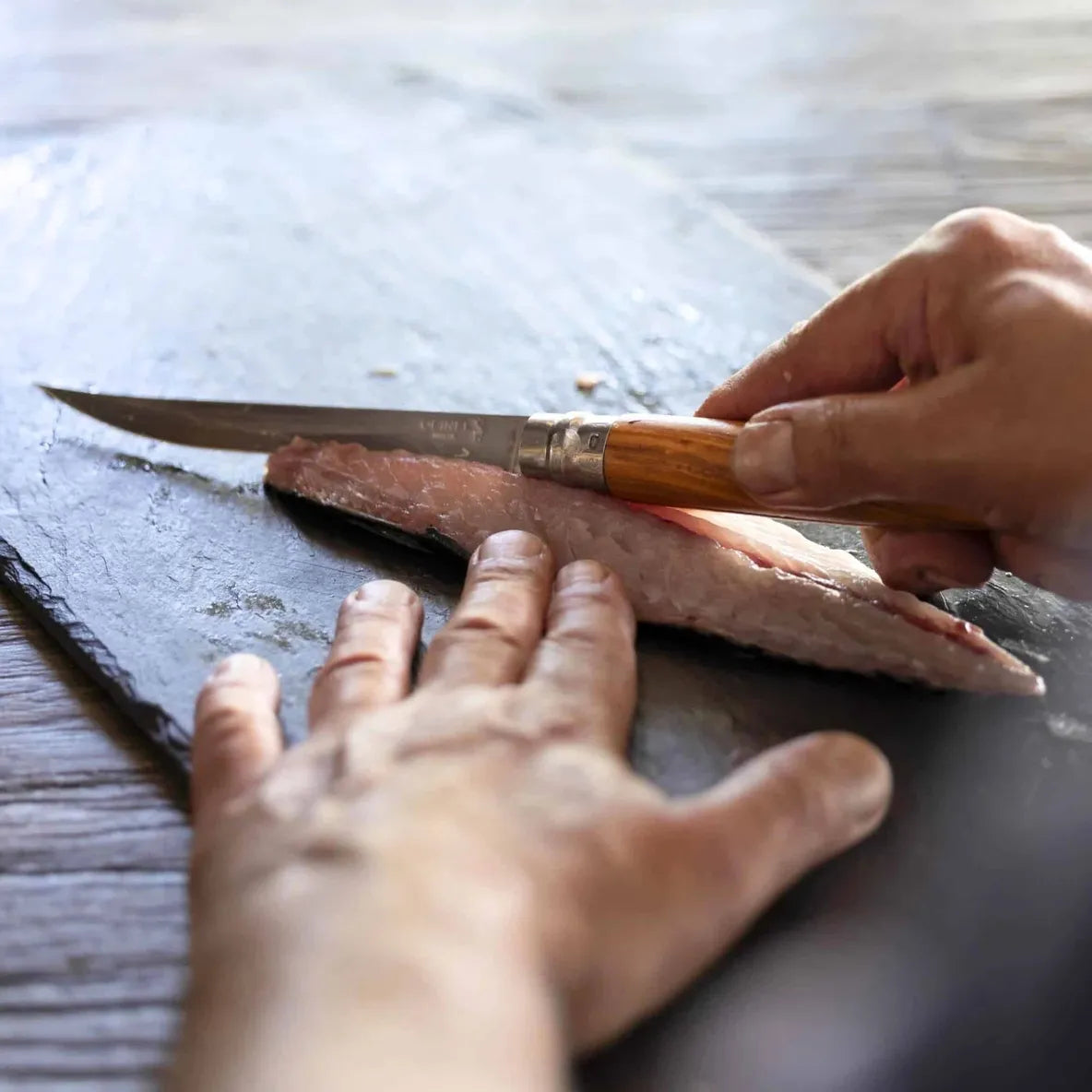 Person cutting fish with an Opinel #12 fillet knife on a wooden board