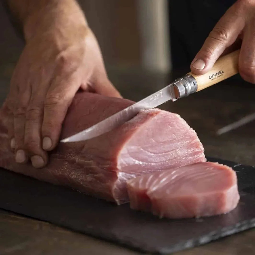 Person cutting a piece of raw fish with an Opinel #15 fillet knife on a dark surface