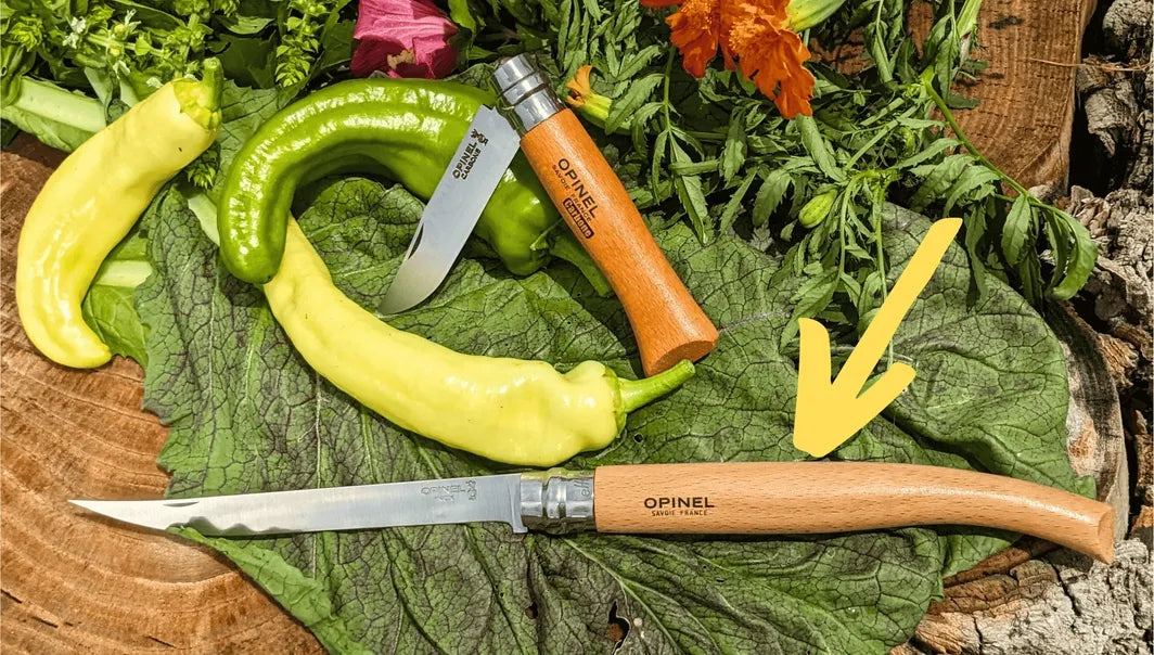 Opinel knives on a wooden surface with green leaves and vegetables
