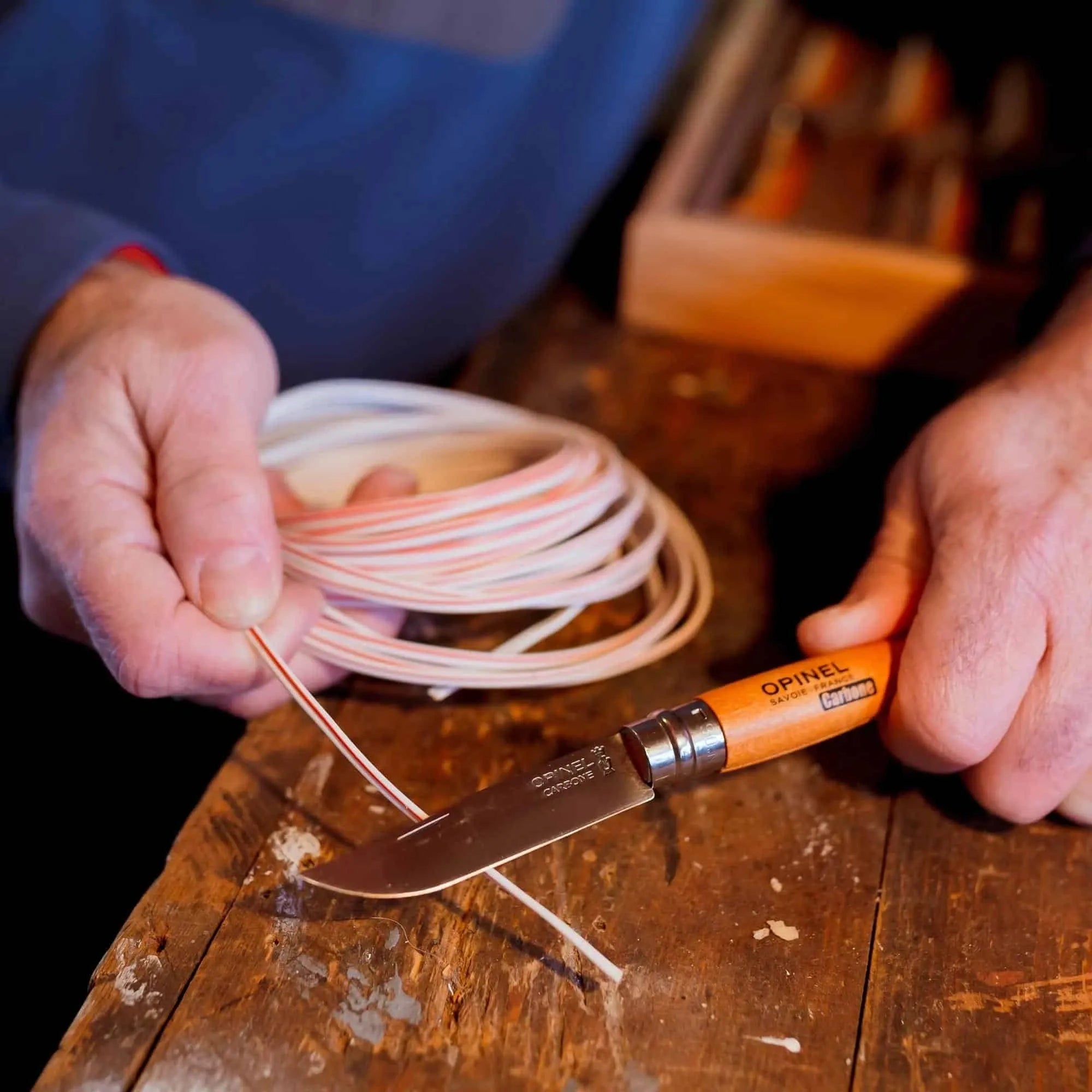 Person using an Opinel #6 carbon folding knife to cut wire on a wooden table