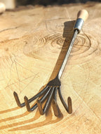 Crow's Foot Garden Tool, Hand Forged "The Claw", tool is flipped on it's back on wooden background. 