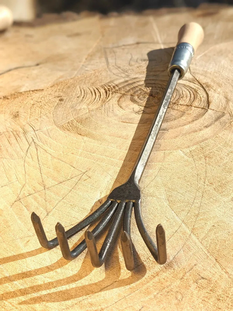 Crow's Foot Garden Tool, Hand Forged "The Claw", tool is flipped on it's back on wooden background. 