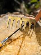 Hand Rake hand forged by Homestead Iron with bright sunlight on steel with harsh shadows on wooden background. 
