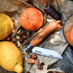 Opinel #8 folding carbon knife on a wooden surface with lemons, oranges, and nuts.