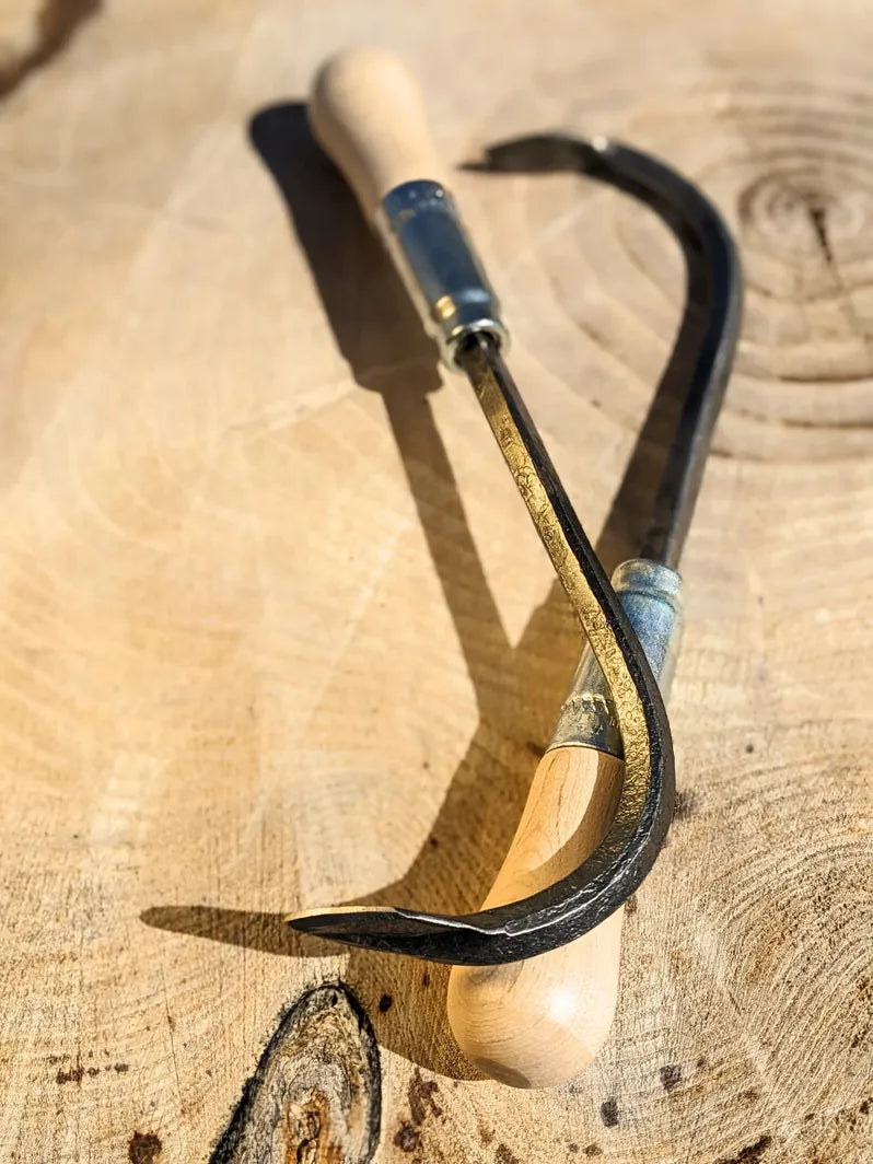 Single Tine Cultivator, Hand Forged Garden Tool by Homestead Iron with bright sunlight on wooden background. 
