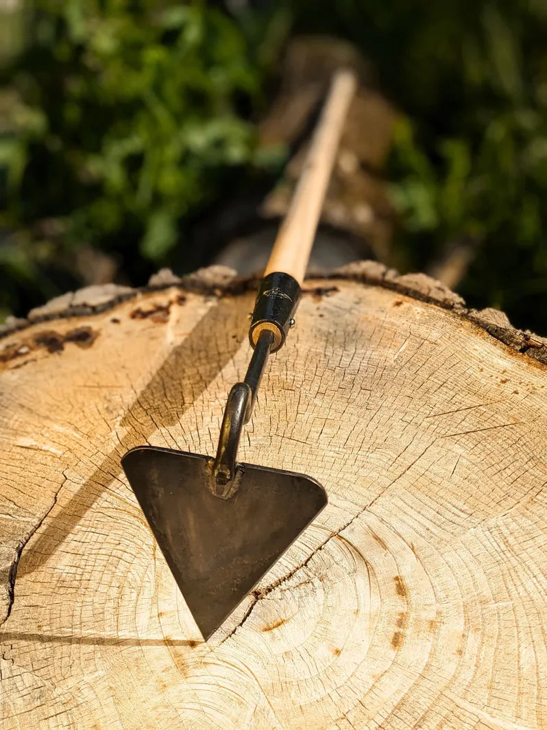 V-Hoe Aggressive Long Handled Hand Forged Hoe Homestead Iron focus on tool head on wooden background. 