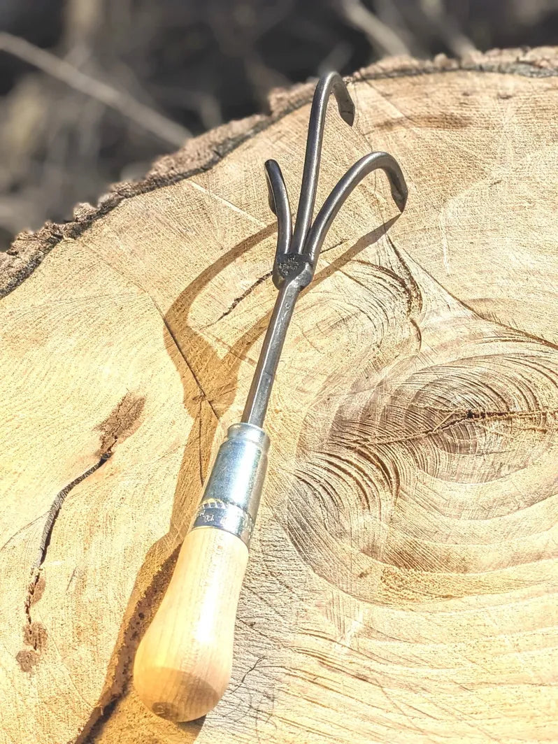 3 Tine Cultivator, Hand Forged Garden Tool, focus on handle on wooden background. 